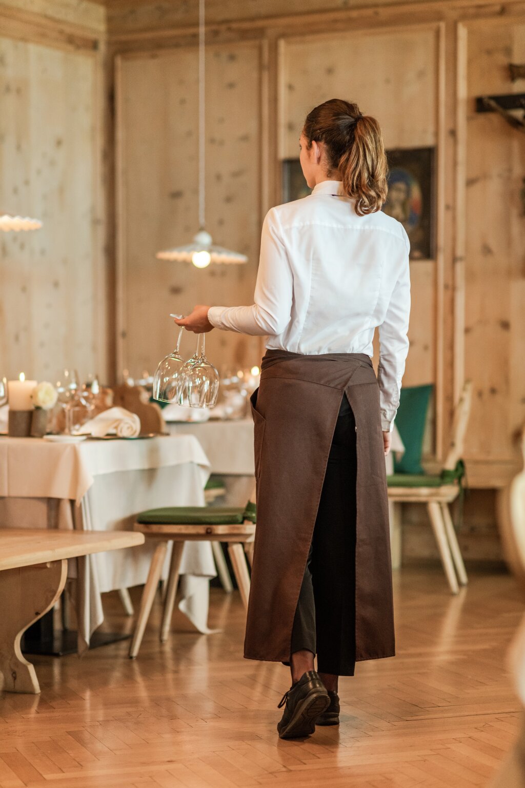 Foto: Armin Terzer Cameriera con grembiule lungo in un ristorante apparecchiato con pareti in legno.